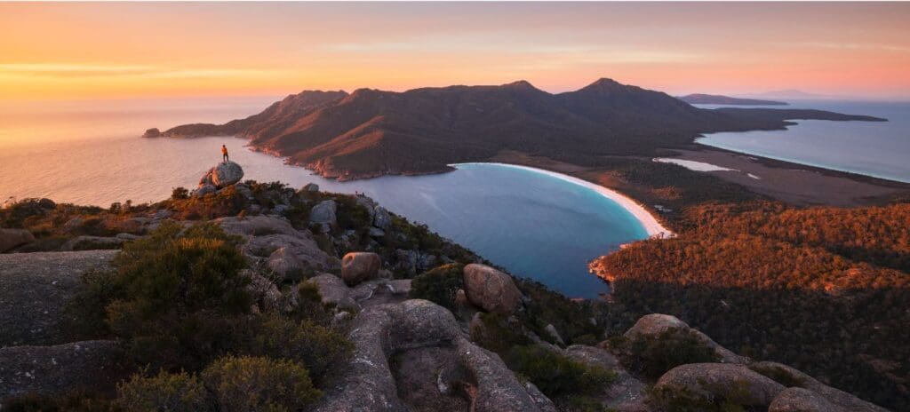 Half-moon bay with a beach surrounded by rugged mountain landscape. Sunset sky with red and orange colors