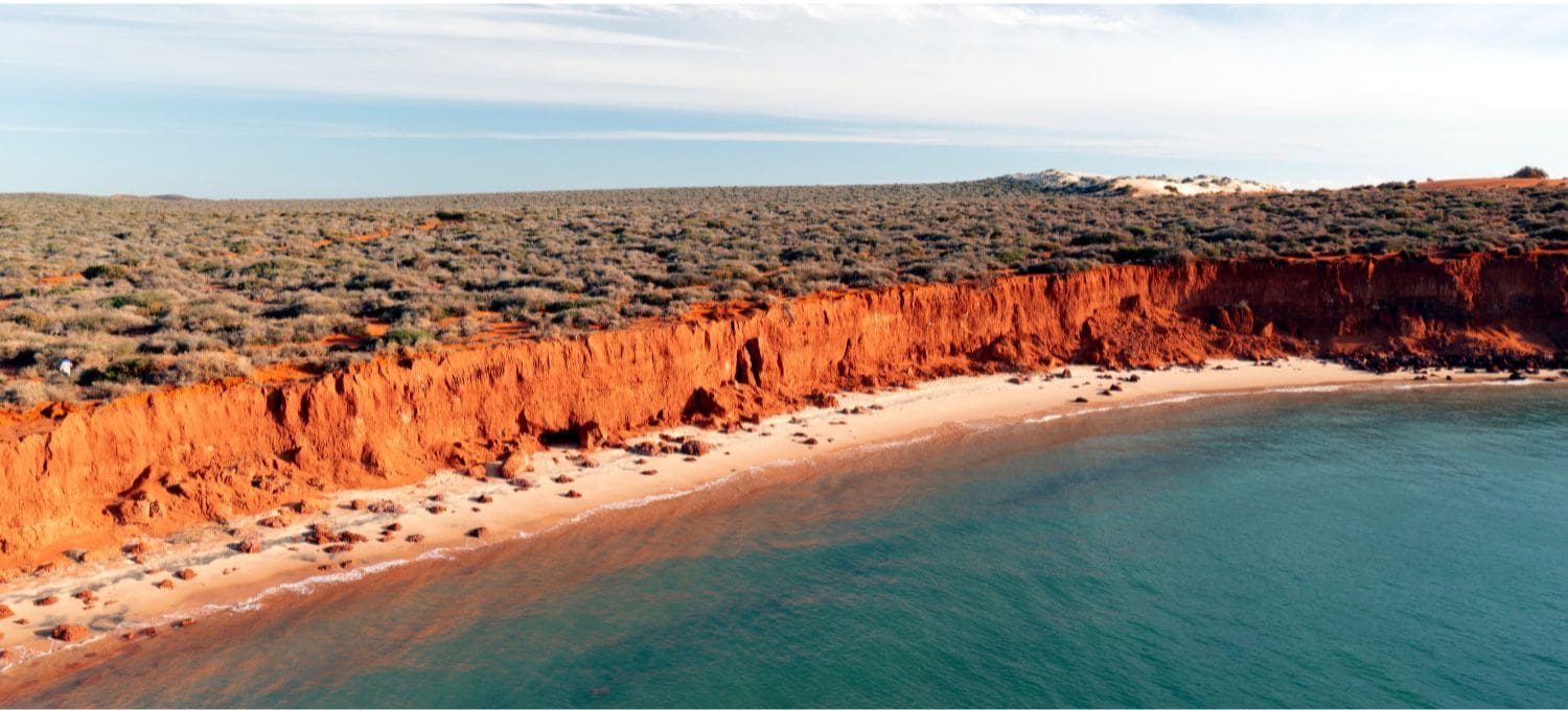 Coastal image with red cliffs, sandy beach and clear ocean water