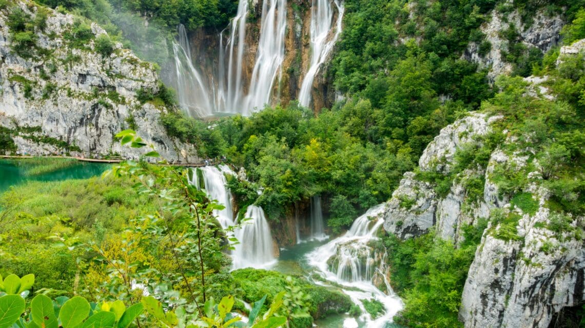 Lush green landscape with cascading waterfalls flowing into turquoise pools, surrounded by rocky cliffs and dense forest, conveying serenity and natural beauty.