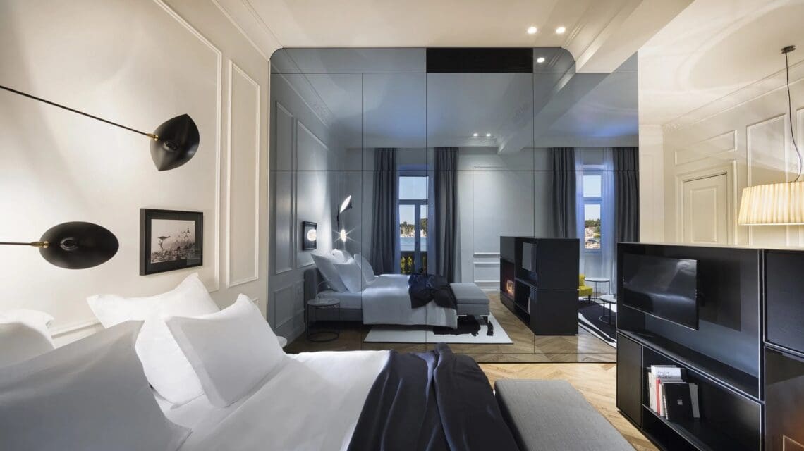 Modern, elegant hotel room with a large mirror reflecting twin beds. Soft lighting, sleek black and white decor, and a cozy atmosphere.