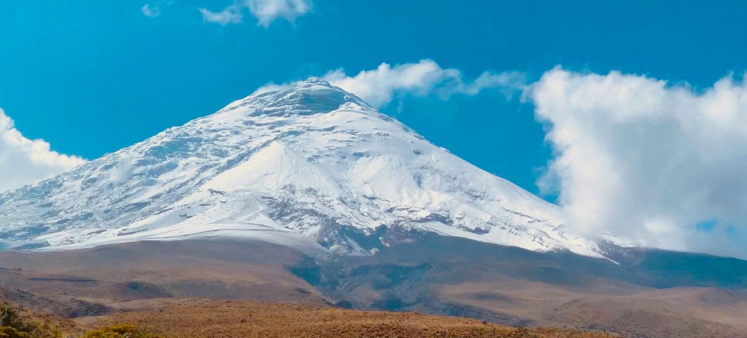 Snow-capped mountain under a bright blue sky with wispy clouds. The rugged peak and serene landscape exude a sense of majesty and tranquility.