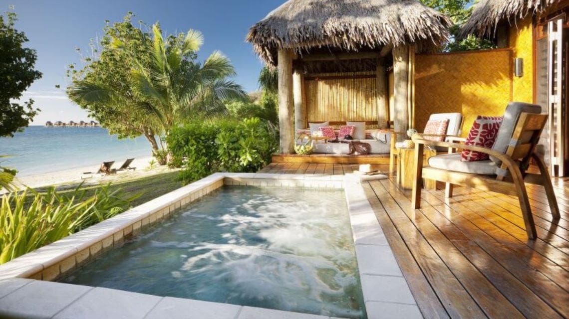 Tropical beachside retreat with a private jacuzzi, palm trees, and ocean view. Wooden deck with comfortable seating, evoking a serene, luxurious vibe.