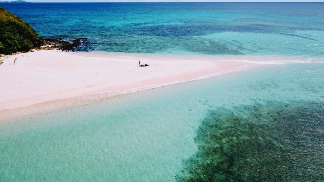 An aerial view of a serene tropical beach with white sand, turquoise water, and a solitary person relaxing on the sand, evoking tranquility and solitude.