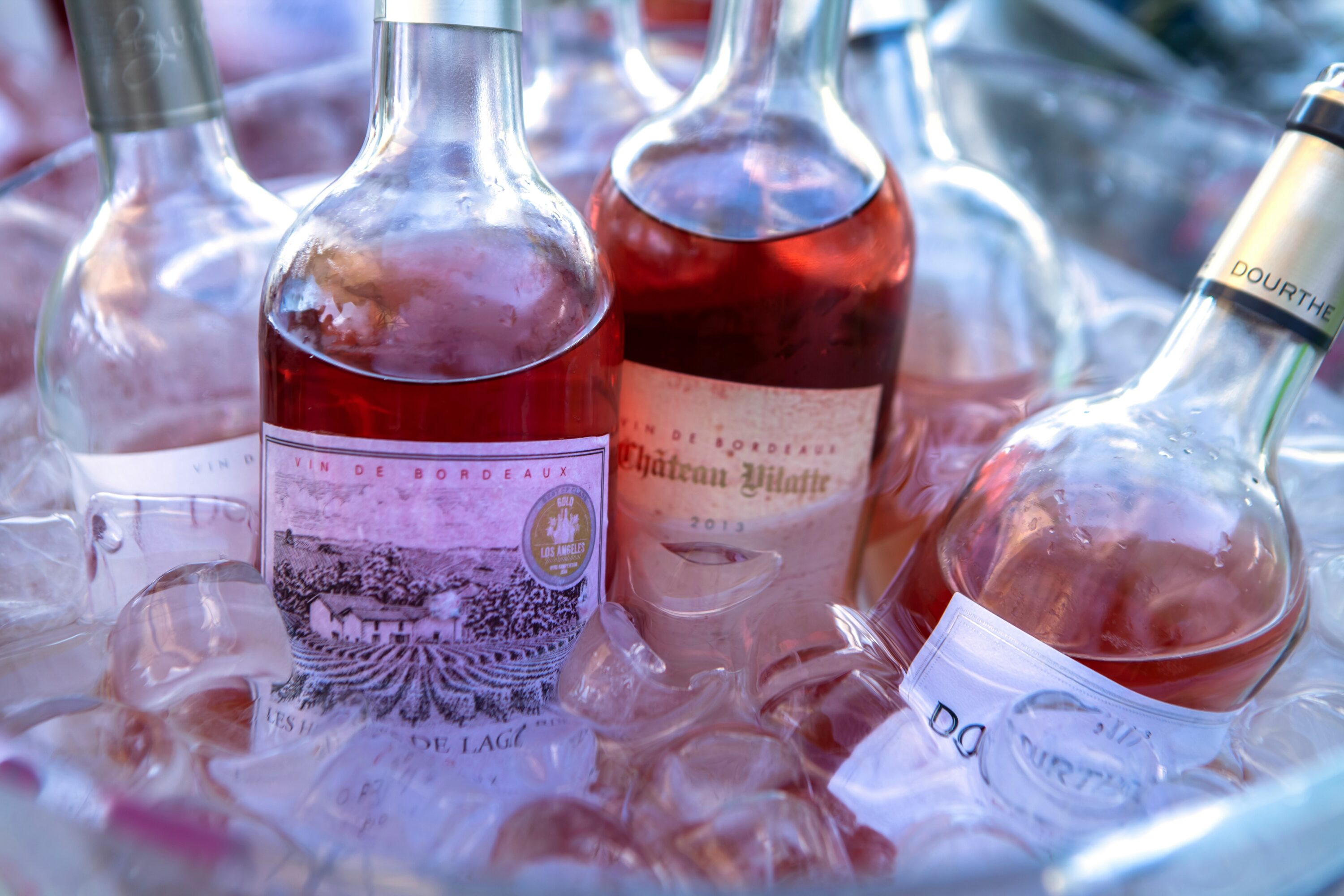 Bottles of rosé wine rest in a bucket of ice, labels visible, evoking a refreshing and sophisticated atmosphere, perfect for a summer gathering.