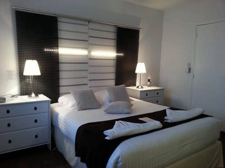 A cozy hotel room with a neatly made bed, adorned with a dark throw and white towels. Soft lighting from two bedside lamps creates a warm ambiance.