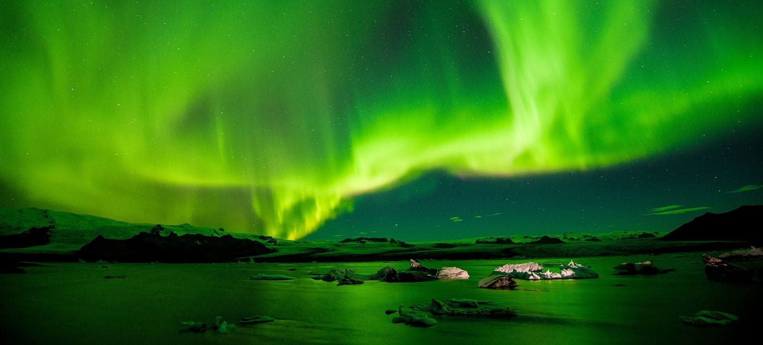 Vibrant green Northern Lights dance across a starry night sky above a serene, icy landscape. The scene evokes awe and natural wonder.