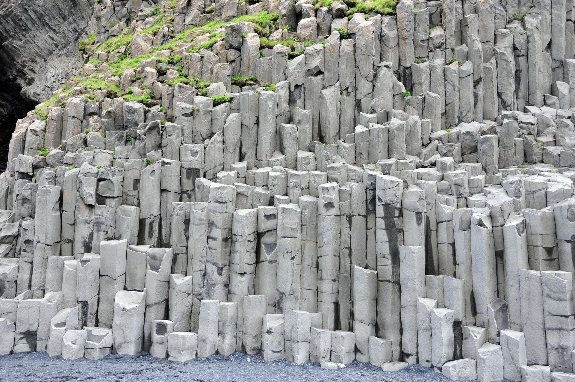 Basalt columns form a striking geometric pattern on a cliff face. The gray stones are topped with patches of green vegetation, conveying a rugged natural beauty.