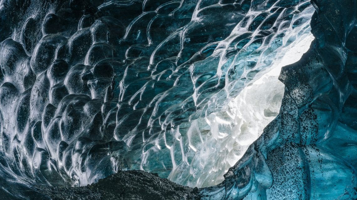 Close-up of a textured blue ice cave interior with intricate patterns and natural light filtering through, creating a serene and mystical ambiance.