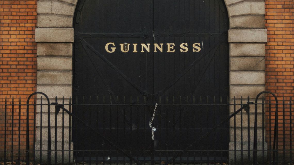 A large black gate with "Guinness" written in bold, cream letters is framed by brick walls and stone pillars, conveying a historic, industrial feel.