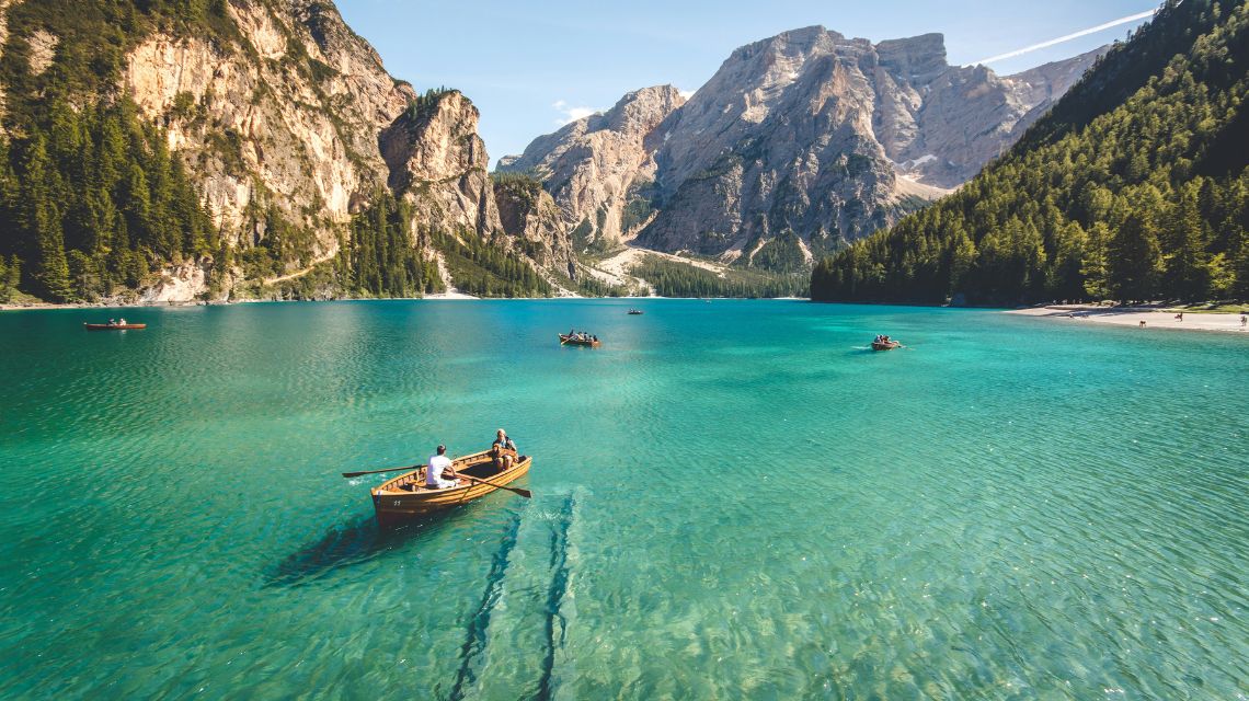 A serene mountain lake with crystal-clear turquoise water. Several small boats with people rowing are scattered across the lake. Majestic mountains and lush green forests form the backdrop, creating a tranquil and picturesque scene.