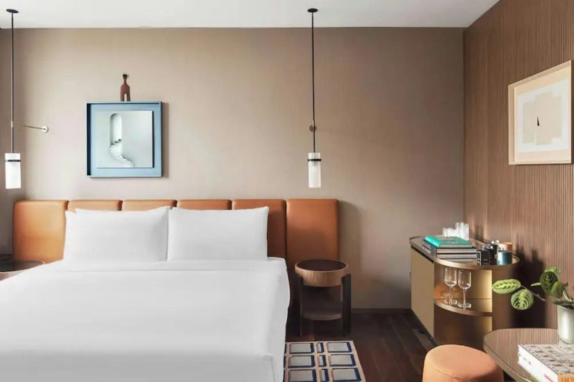 Modern hotel room with a neatly made bed, tan leather headboard, pendant lights, and minimalist decor. Cozy, contemporary, and inviting ambiance.