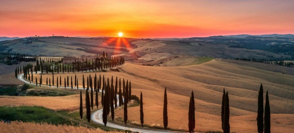 Sunset over Tuscan hills features a winding road lined with tall cypress trees, golden fields, and a vibrant orange sky, evoking tranquility.