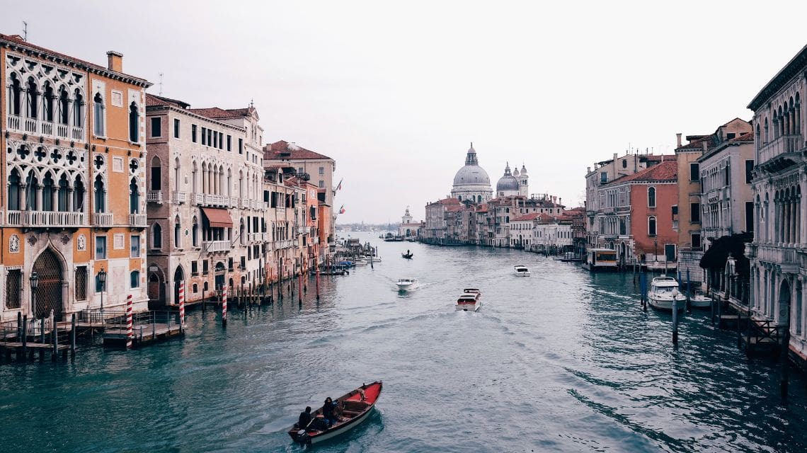 Scenic view of Venice's Grand Canal with historic buildings on both sides. Boats glide along the blue-green water, evoking a calm, picturesque ambiance.