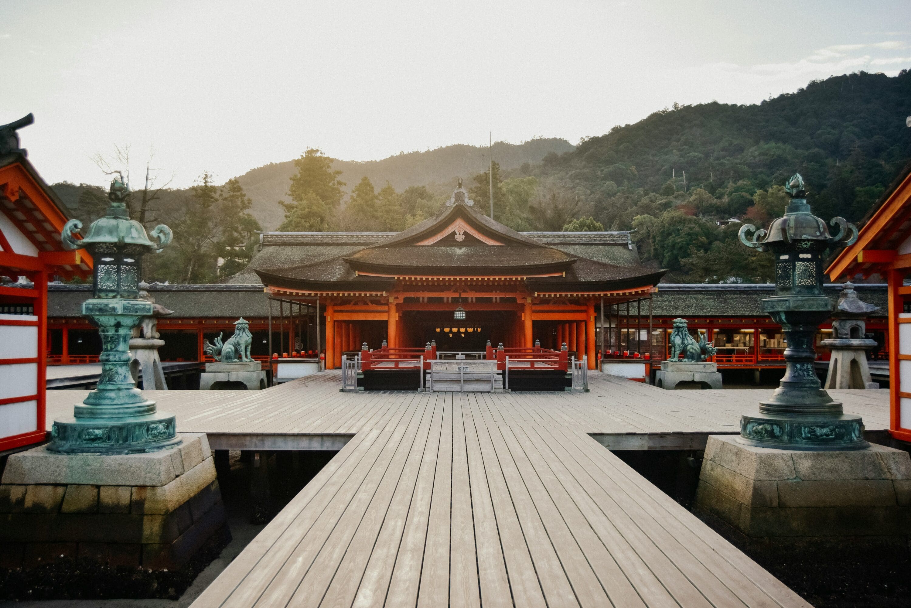 A serene Japanese shrine with vibrant red structures stands against a backdrop of lush green hills under a clear sky, conveying tranquility and harmony.