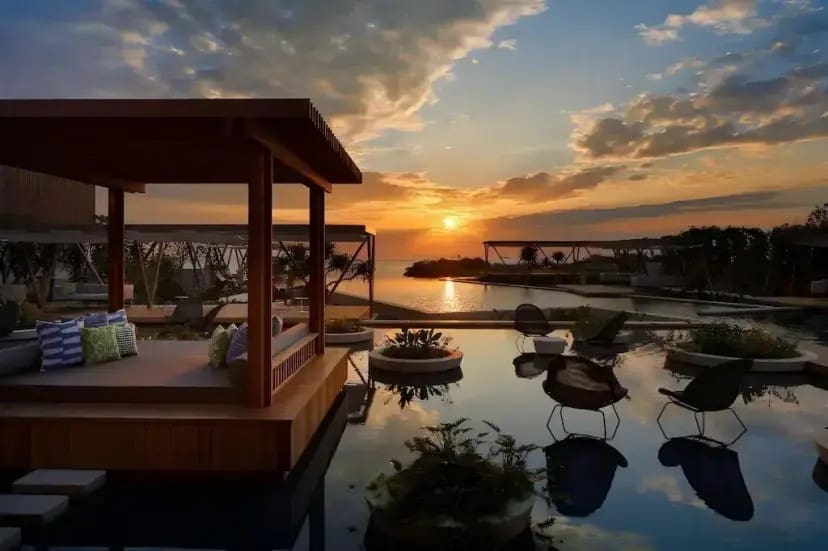 Luxurious seaside resort at sunset, featuring an outdoor lounge pavilion with cushions, pool reflections, and a serene, inviting atmosphere.