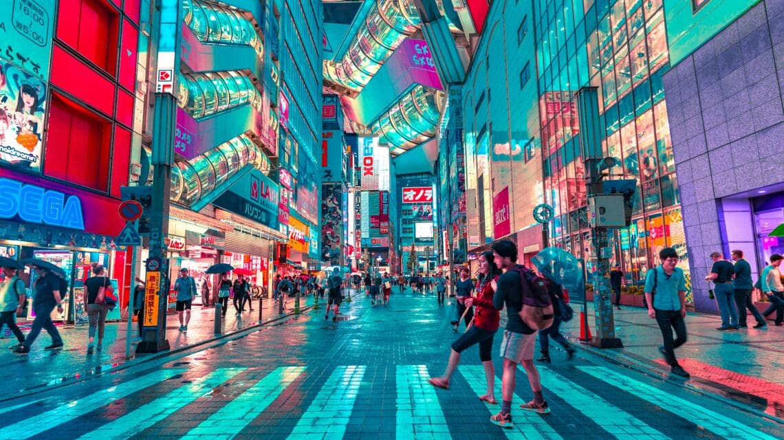 Bustling city street at night, filled with people crossing, vibrant neon signs, and colorful reflections on wet pavement, conveying lively energy.