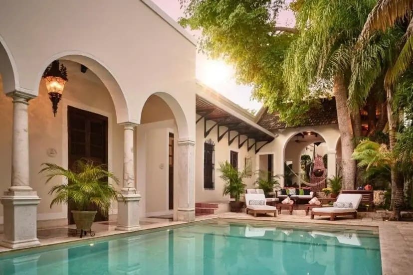 Luxurious courtyard with a serene pool, framed by elegant arches and lush greenery. Sunlight filters through trees, creating a tranquil ambiance.