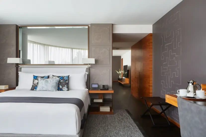 Modern hotel room with a large bed, white linens, and blue floral pillows. Gray walls with geometric designs create a calm, sophisticated ambiance.
