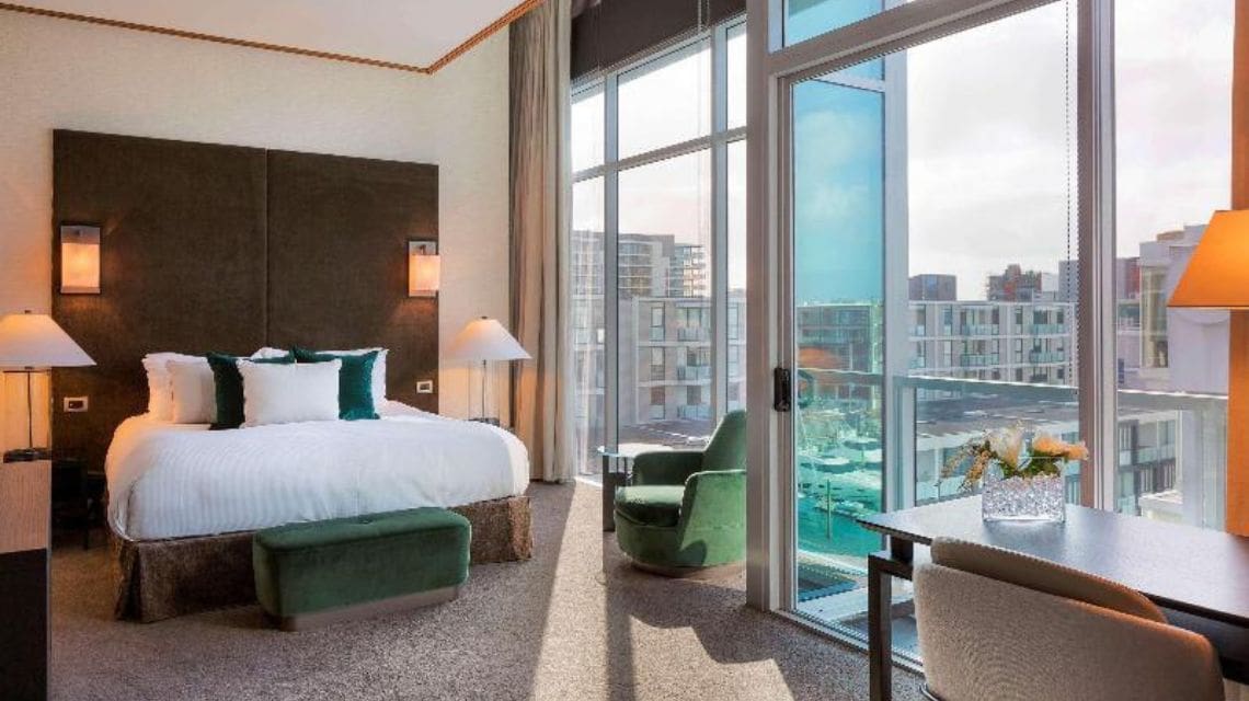 Interior hotel room with a large bed next to a wall of windows