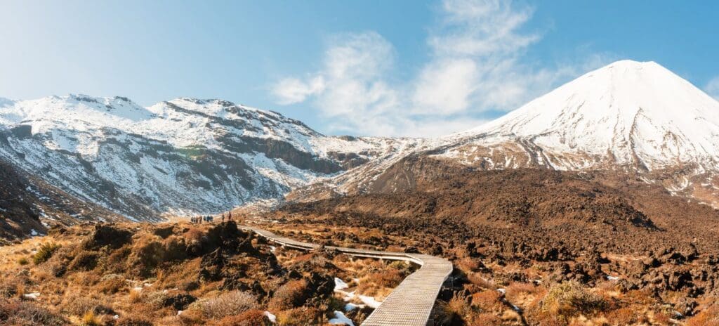 Wooden boardwalk leading through rugged terrain with snow-capped mountains in the background