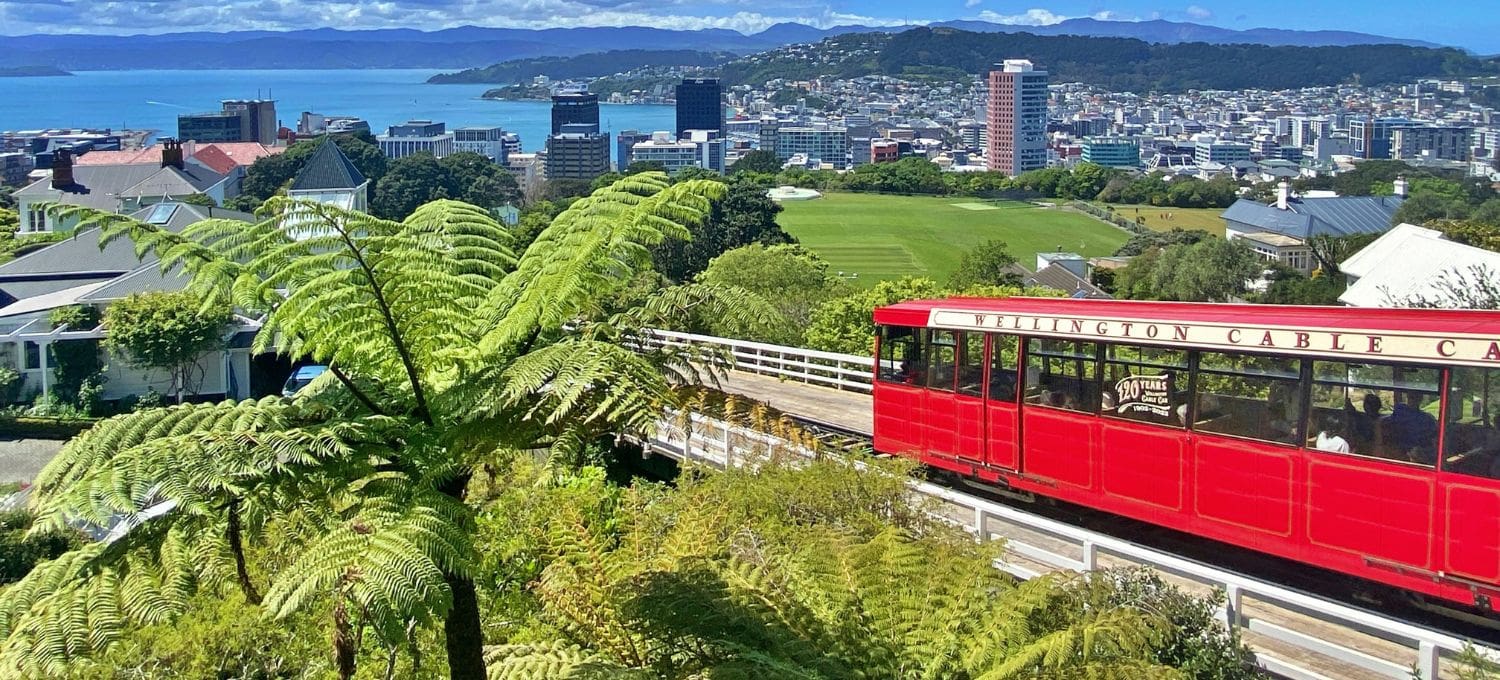 Red cable car traveling up a steep hill side with the skyline of a small city in the background