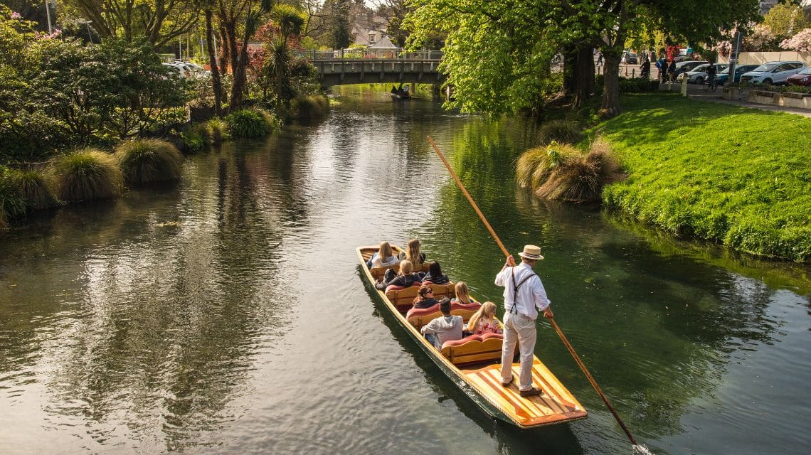 Punting boat on a canal heading towards a bridge over the canal with lush vegetation on the sides of the canal