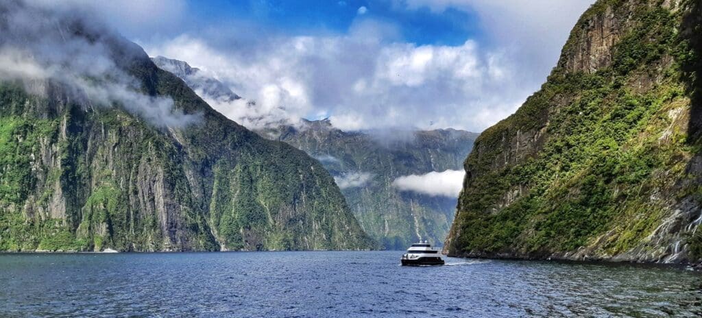 Boat crusing through a fiord with steep mountains boarding surrounding the water