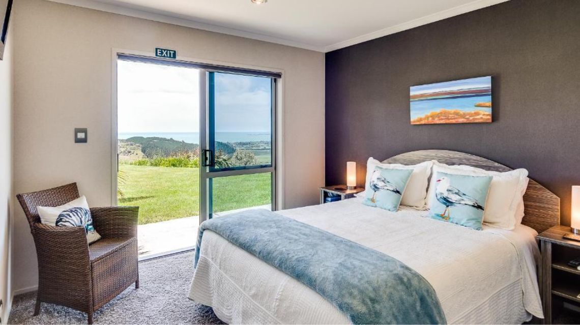 A cozy bedroom with a double bed features ocean-themed decor. An open glass door reveals a scenic countryside view, creating a tranquil atmosphere.