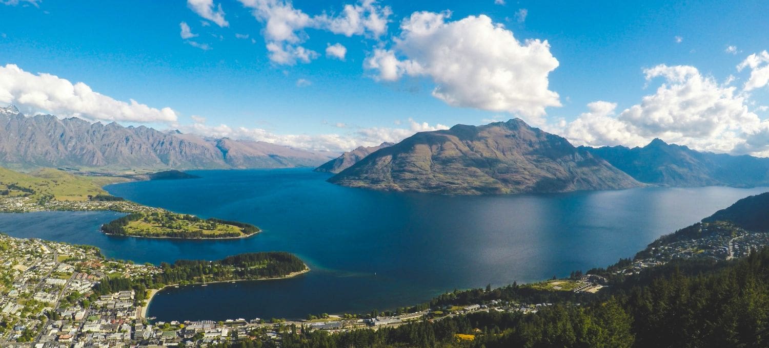 Aerial view of a small town nestled next to a large lake with rugged mountains in the background