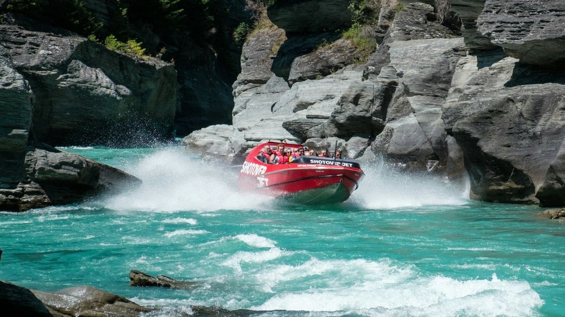 Red jet boat gliding across the top of a river in a narrow canyon