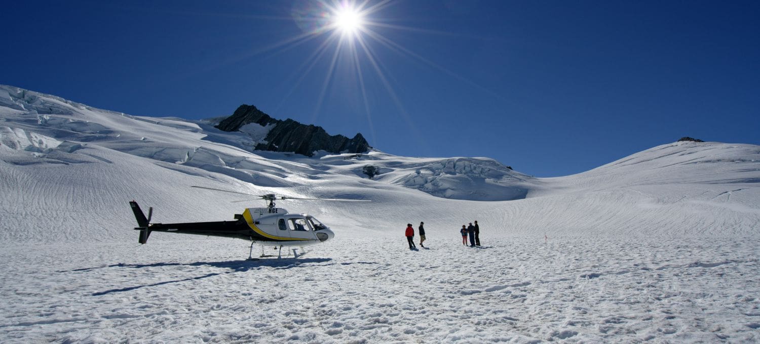Helicopter on a glacier, with three people near by standing on the glacier
