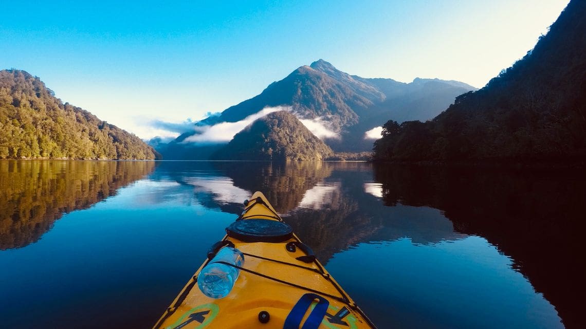 Tip of a kayak on a lake with rugged mountains in the background