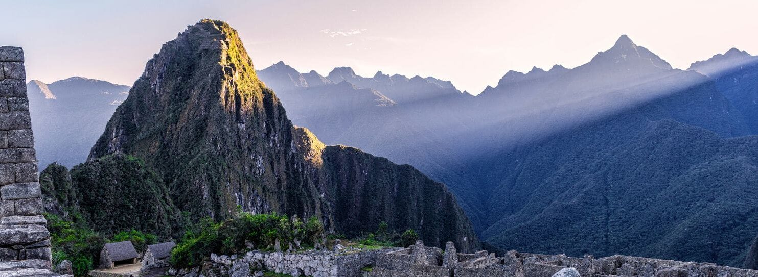 Sunrise over Machu Picchu, with rays illuminating the ancient Incan ruins and surrounding mountains. The scene is serene and majestic.