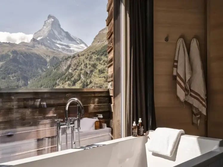 Luxurious bathroom with a freestanding tub, soft towels, and toiletries. Large window offers stunning mountain view, creating a serene, inviting atmosphere.
