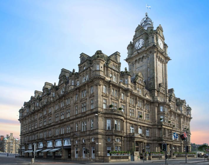 Ornate historic building with a grand clock tower under a clear blue sky. The architecture is detailed and majestic, conveying elegance and timelessness.