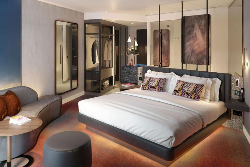 Modern hotel room with a large bed featuring pillows and a soft headboard, a cozy sofa, round table, and open wardrobe. Soft, warm lighting sets a relaxing tone.
