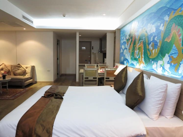 Modern hotel room featuring a king-sized bed, stylish decor, and a vibrant dragon mural, with a seating area and dining space.