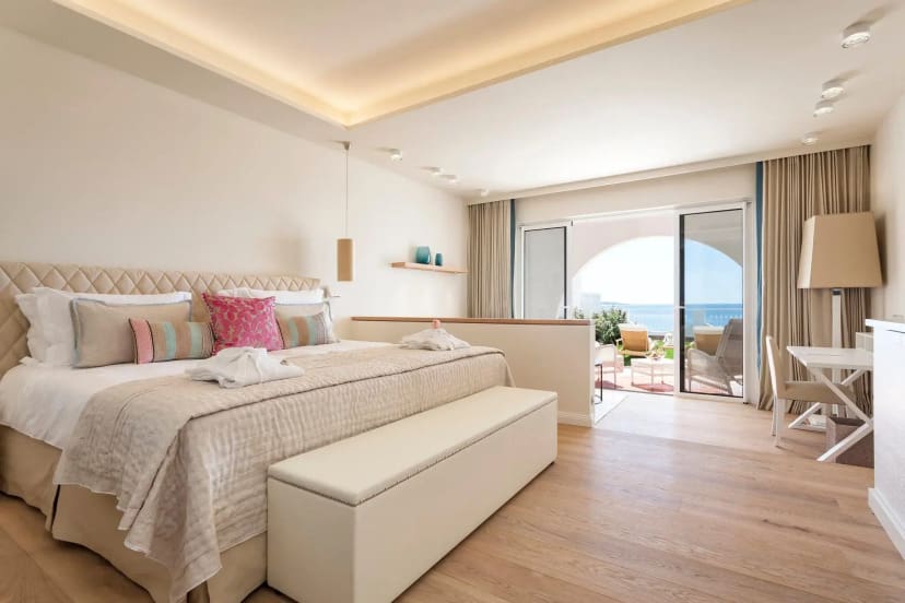 Stylish room in neutral tones with a large bed, and sliding door to an outdoor space with a view of the ocean