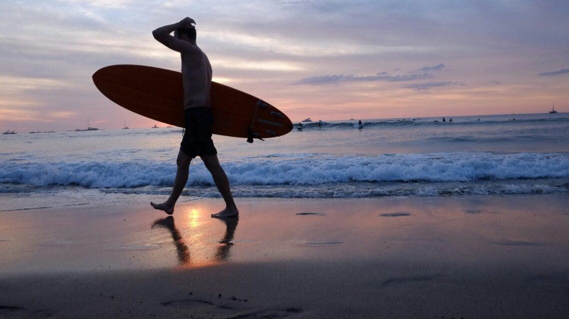 a-man-walking-on-a-beach-holding-a-surfboard