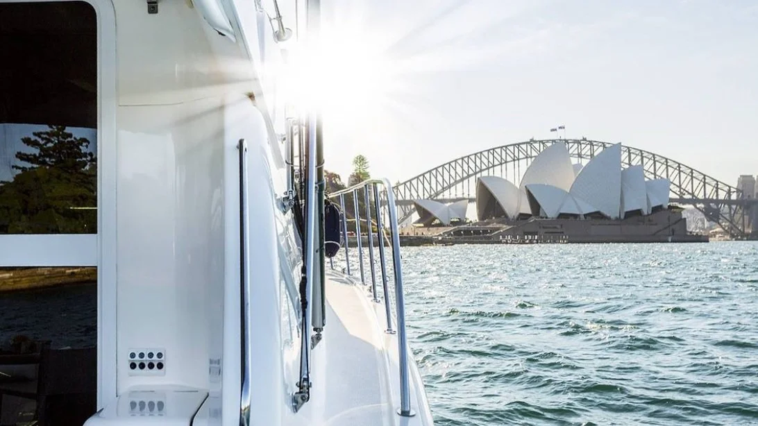 View of the Sydney Opera House from a boat on the harbor, with the Harbour Bridge in the background.
