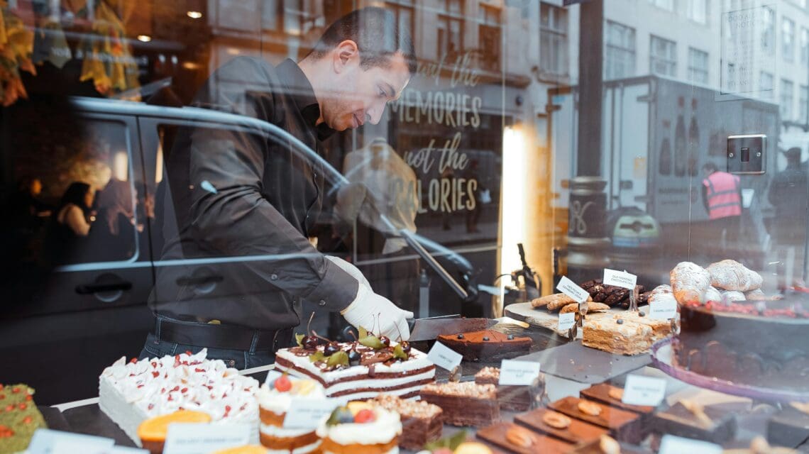 cake display in a window with worker setting down new desserts