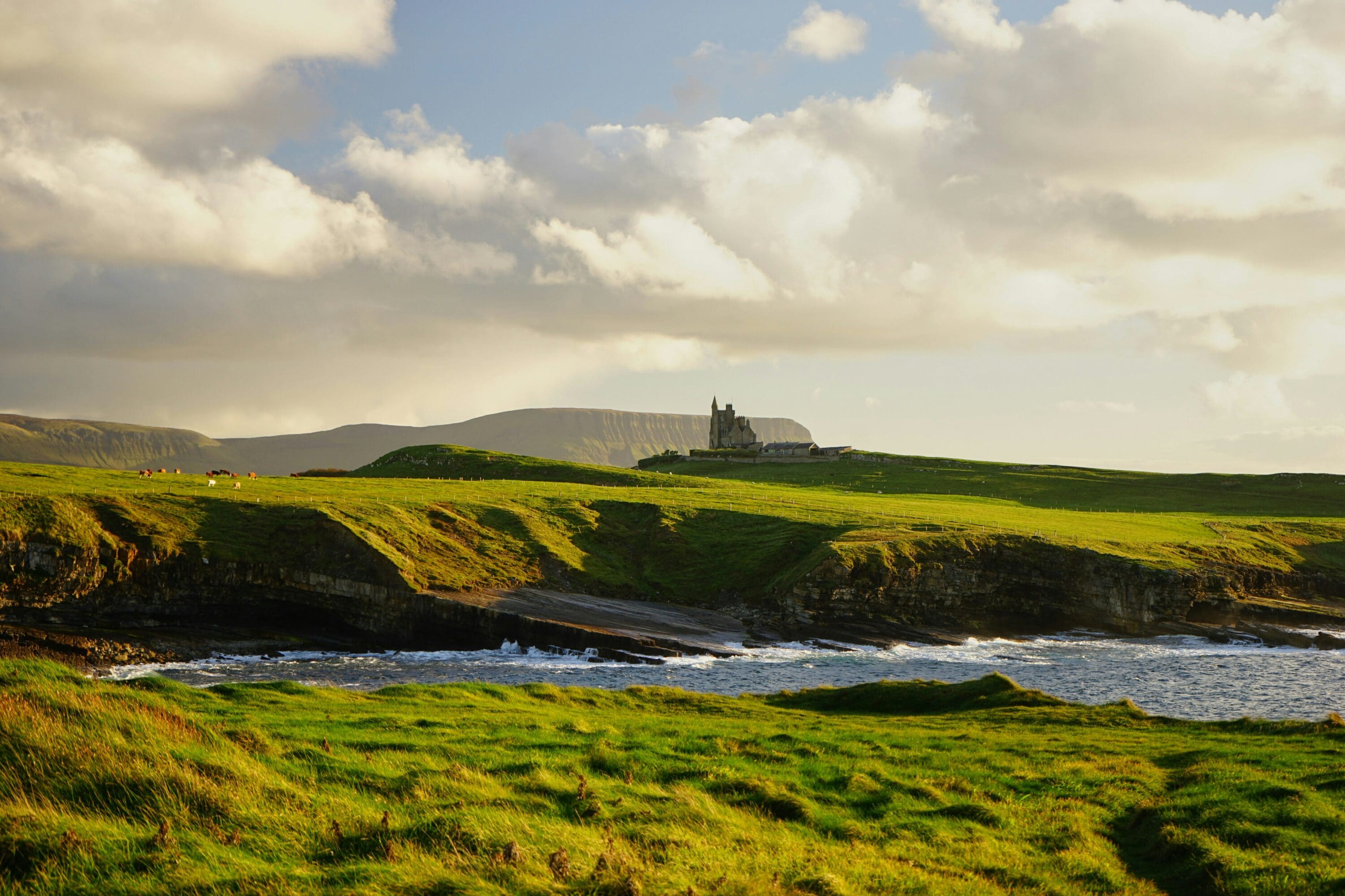 Castle in the distance on a rocky coast with lush green landscape
