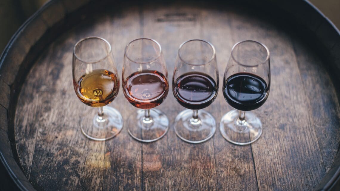 small glasses with small amounts of dark port wine on top of a wooden barrel