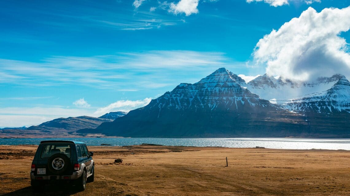 SUV parked in a grassy field with a rugged mountain in the background