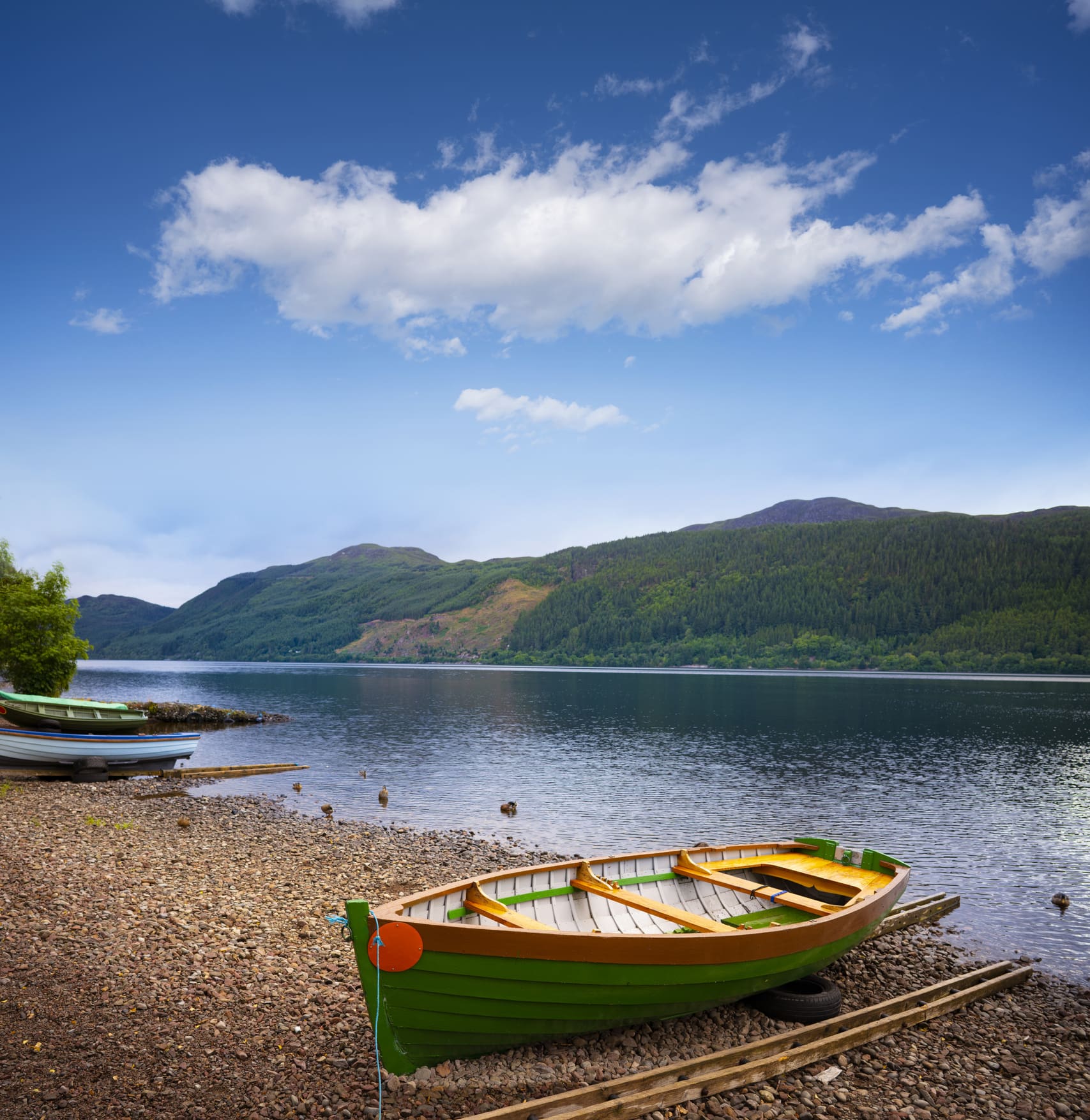 Row boat sitting on the rocky shore of a lake with rolling hills in the background