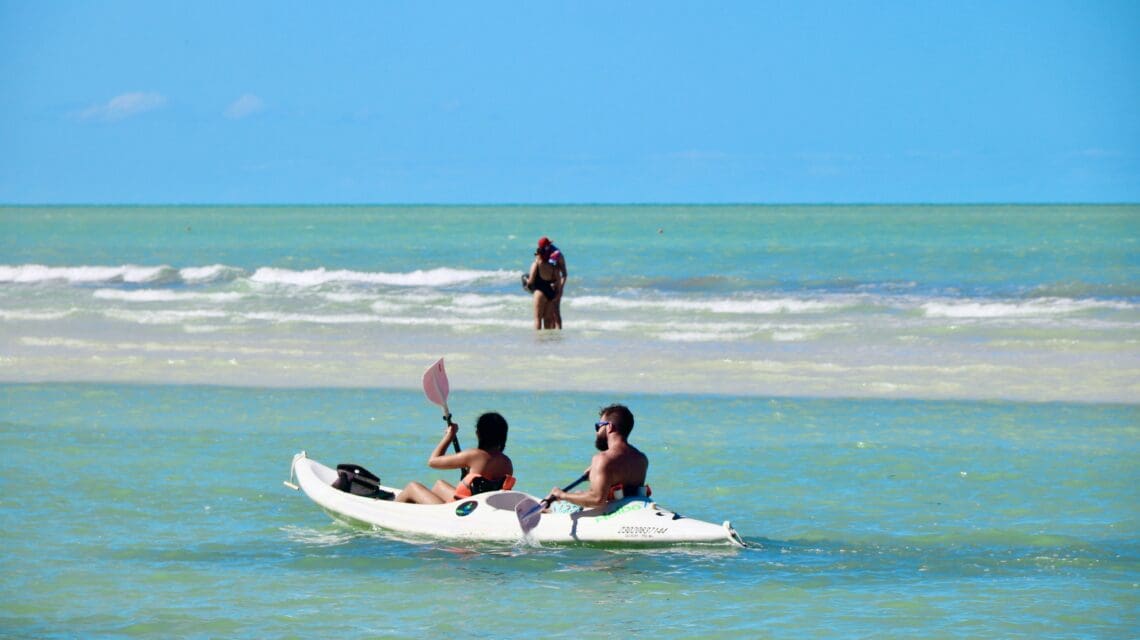two people in a kayak in clear blue ocean water under a cloudless sky