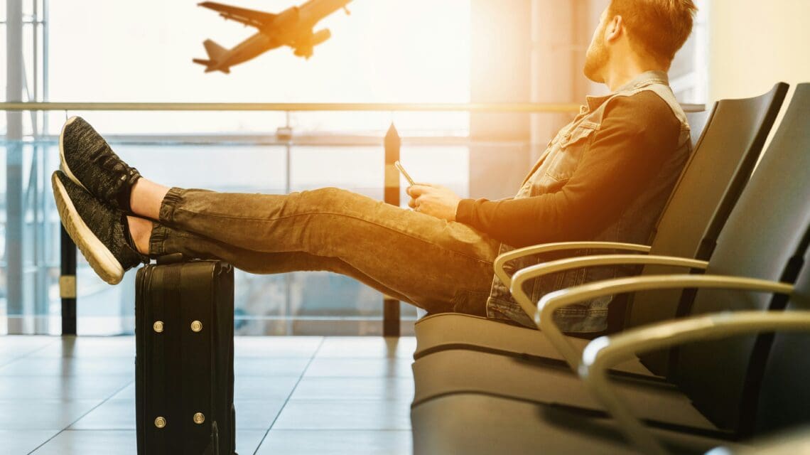 man sitting in a chair at an airport looking out a window watching a plane take off