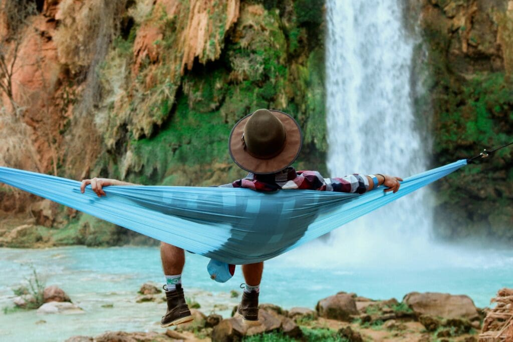 man sitting in a hammock on a rocky beach with a waterfall flowing in the background