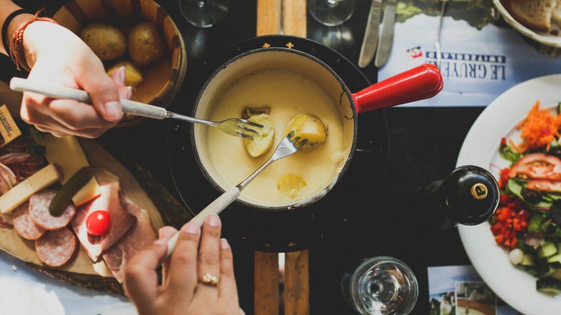 two person holding fork dipping food on sauce