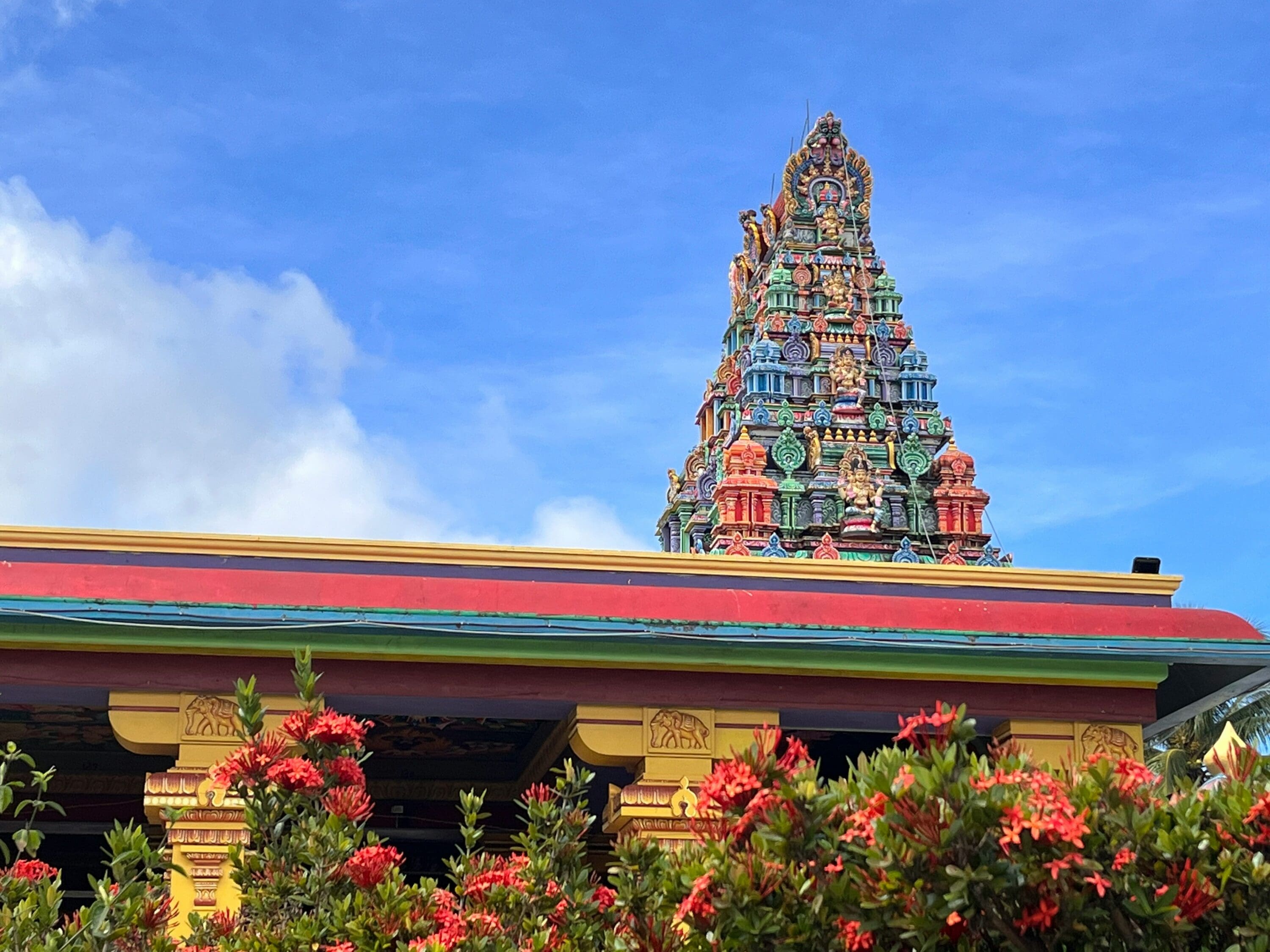 Colorful Hindu temple with blue sky in the background and tropical plants in the foreground